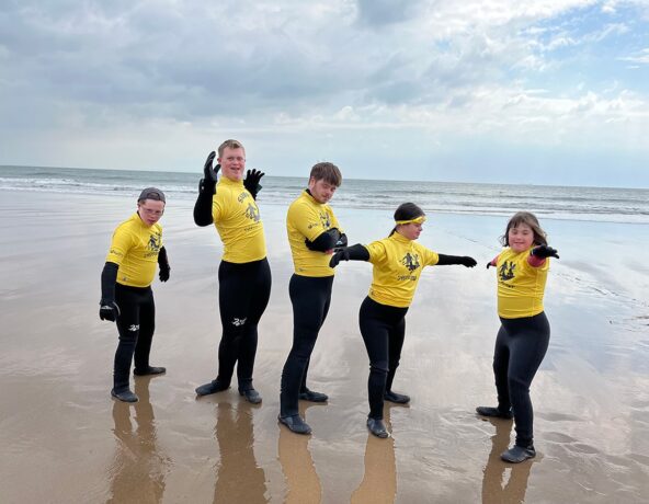 Five children posing on the beach in wetsuits