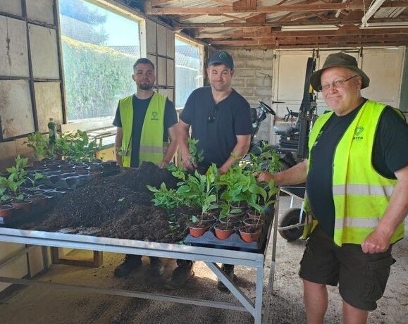 Three individuals standing by a potting table of plants