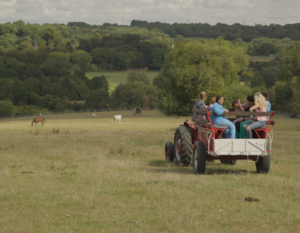 Teenagers sitting in a trailer being pulled by a tractor across a field