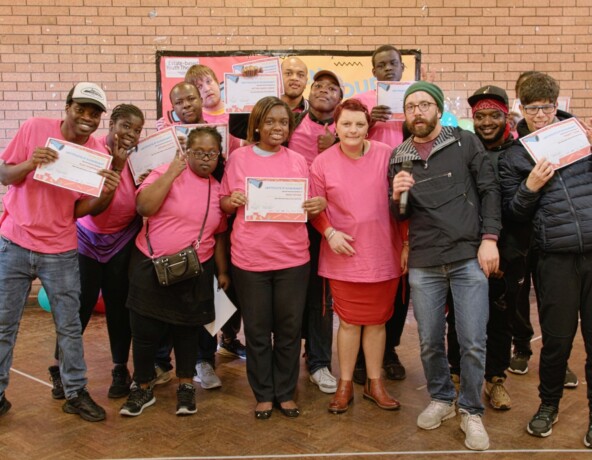 Group of individuals wearing pink t-shirts holding certificates of achievement