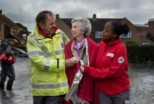 Two aid workers rescuing an elderly lady from flooding.
